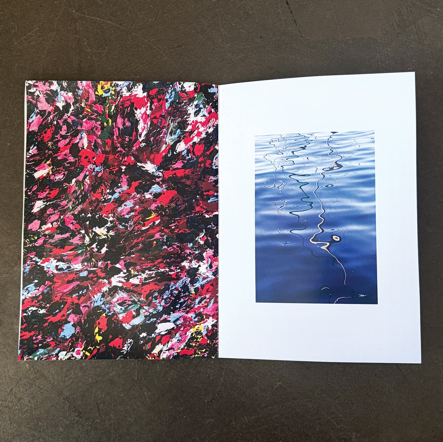 Two zine pages on a concrete surface, one with an abstract multicolor painting and the other with blue water reflection.