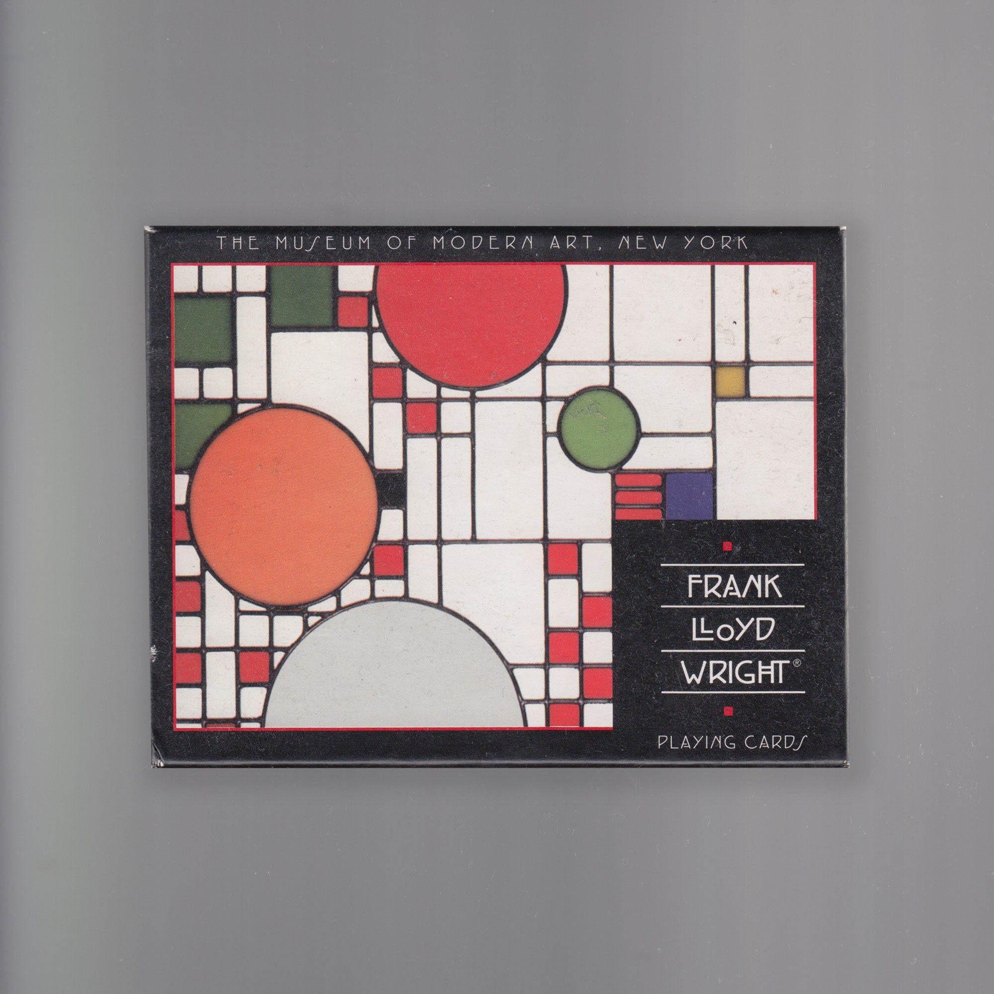 Art deco cover box of Frank Lloyd Wright's playing cards for the Museum of Modern Art, New York. Vibrant red, orange, and green circles and squares adorn the box. Scanned image presented as a square.