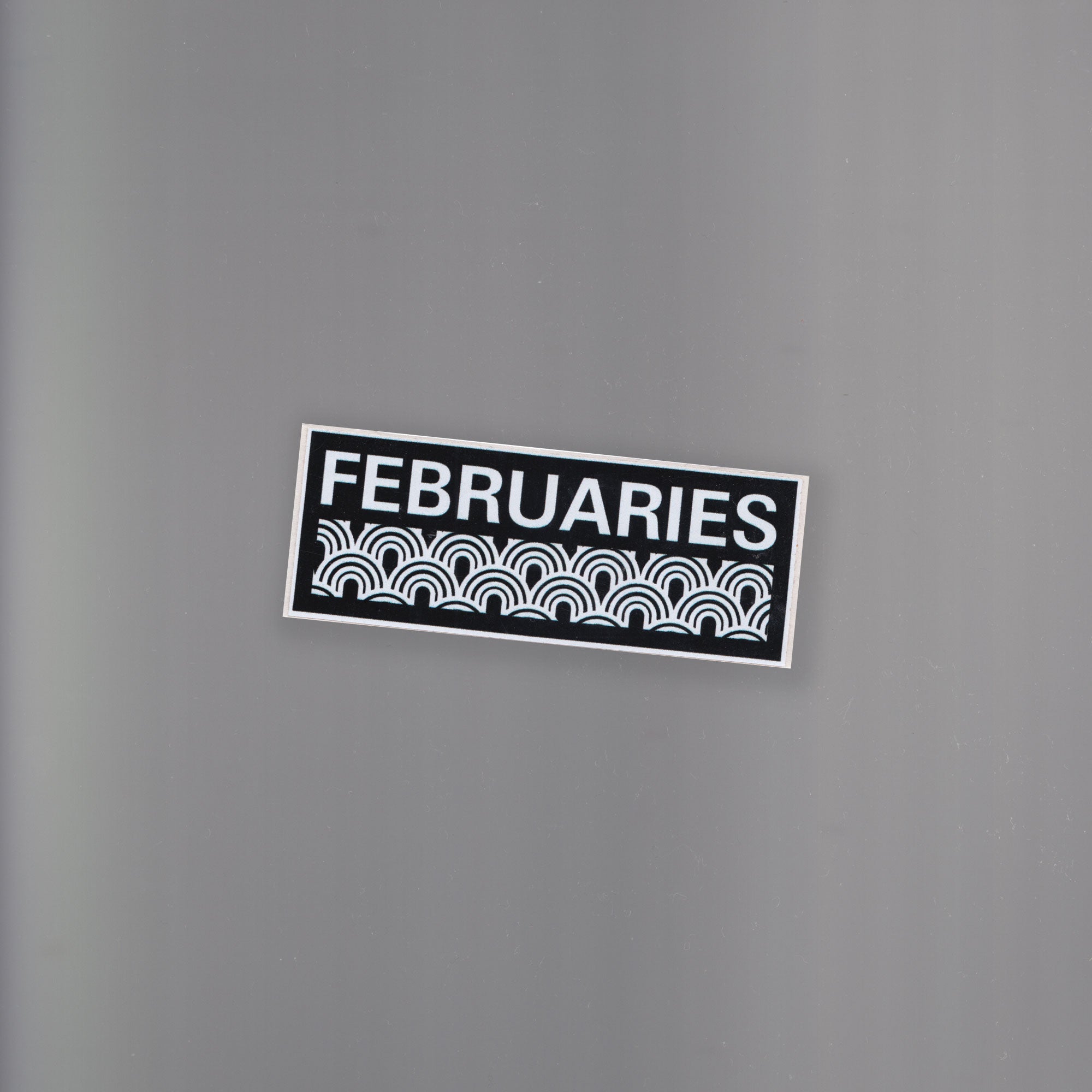 A black and white rectangle sticker graphic with abstract circular shapes and a text logo with the branded word 'FEBRUARIES' in all-caps.