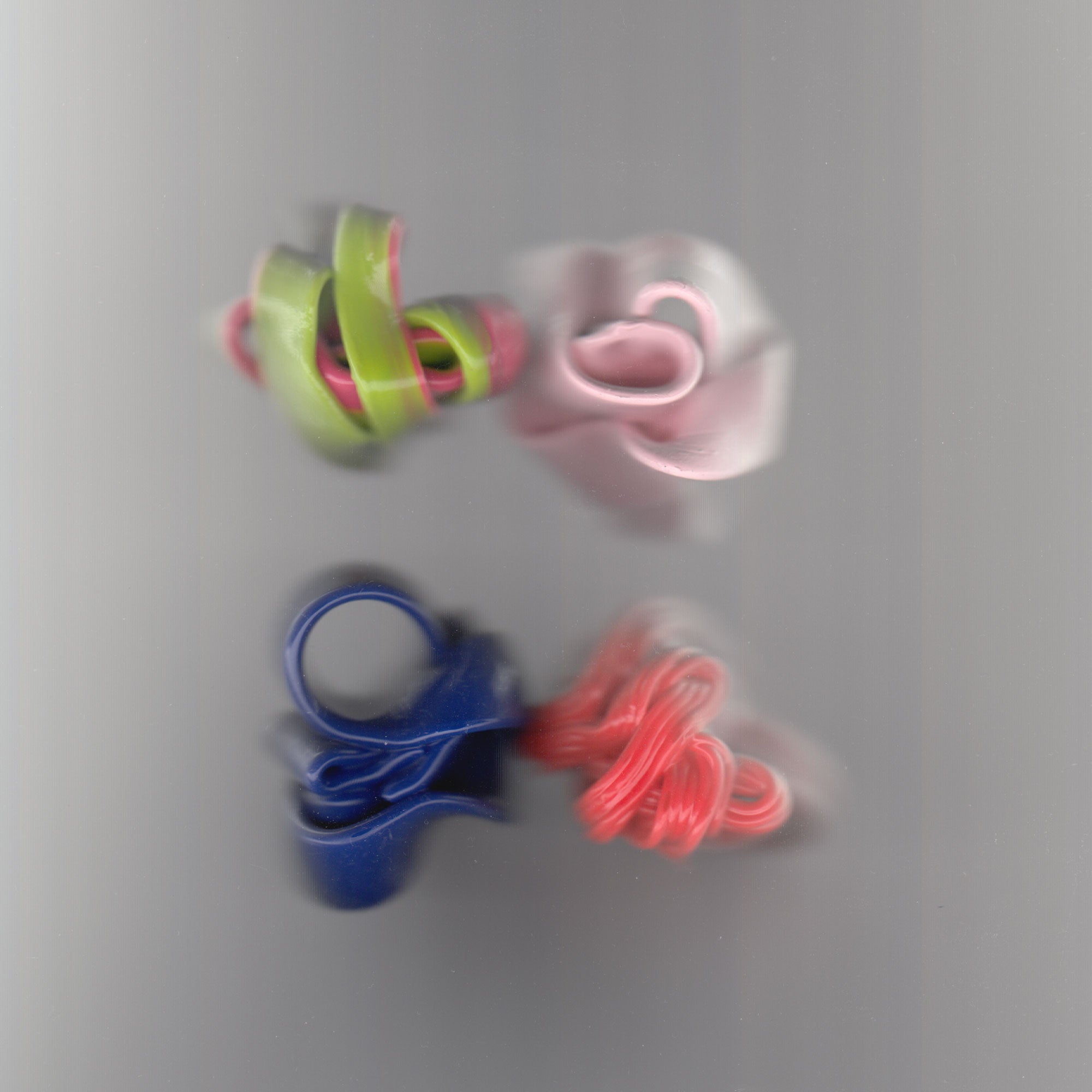 A distorted scanned image of four rings designed by Gaetano Pesce. The colours are vibrant lime green, pastel pink, navy blue and hot orange.