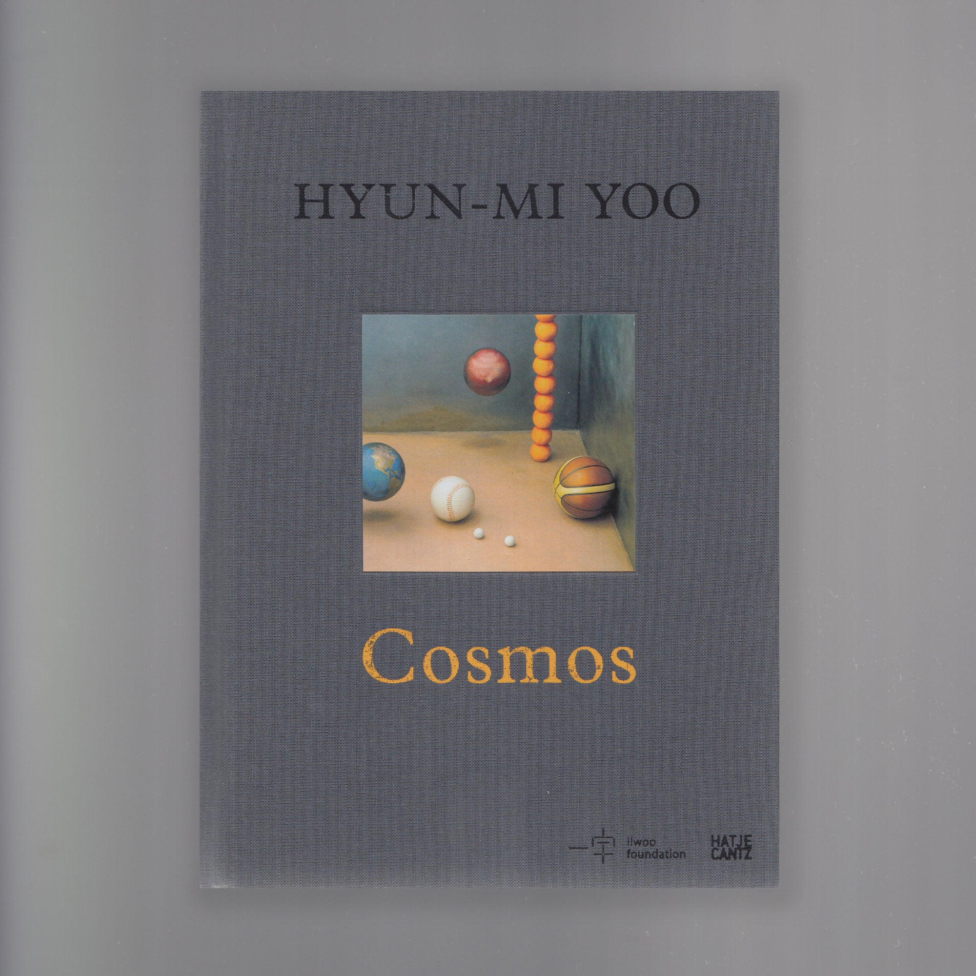 Grey front cover scan of the book "cosmos" by artist Hyun-Mi-Yoo. The front image of the book displays four types of sport balls painted realistically.