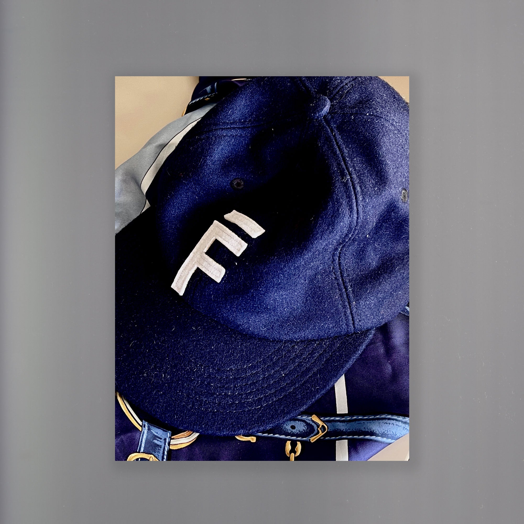 An image of a navy blue wool 6 panel hat with the 'Februaries' logo 'F' stitched onto the front of the hat. A blue Cartier scarf is in the background.