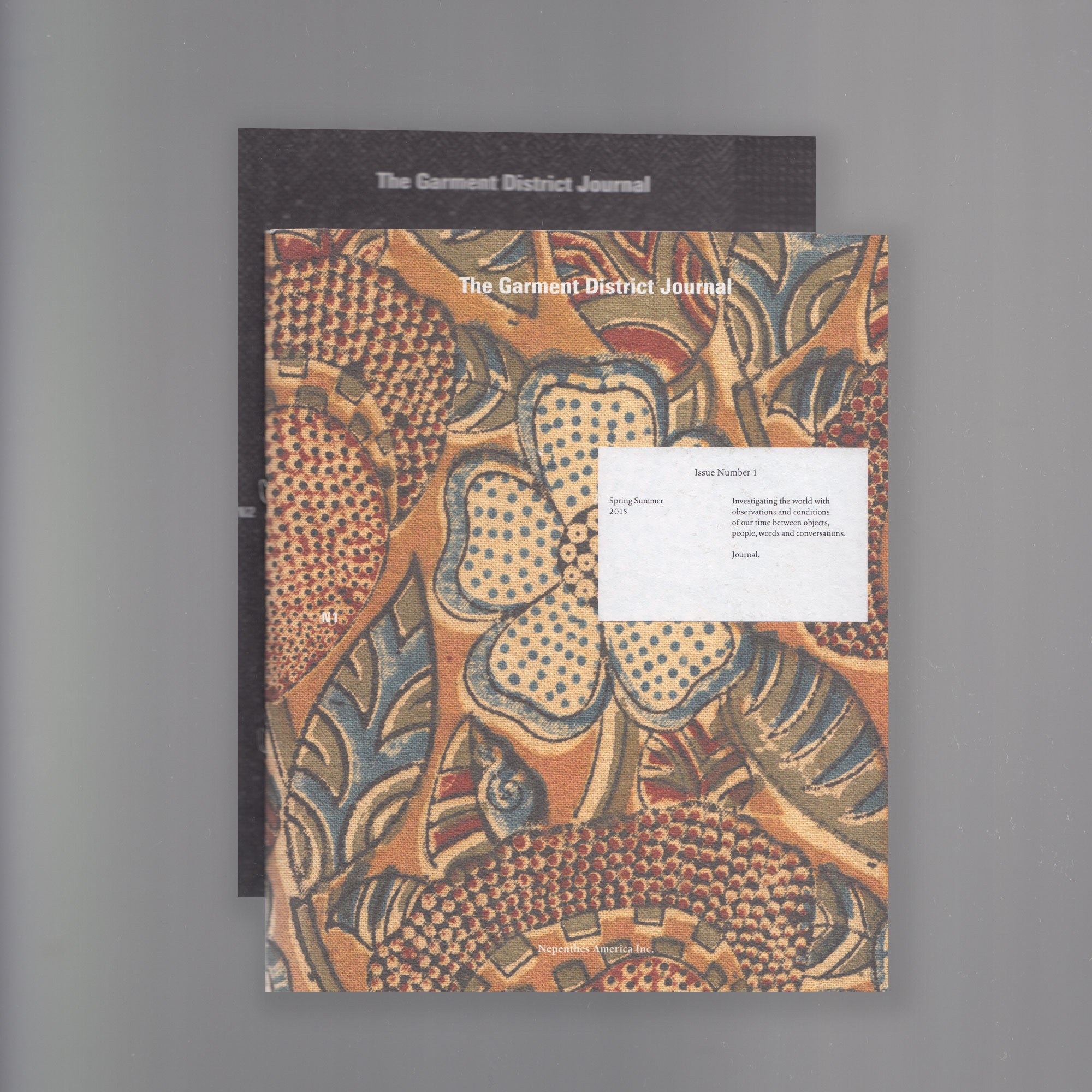 Two booklets displayed with a yellow and brown natural pattern with the text 'The Garment District Journal' displayed on top.